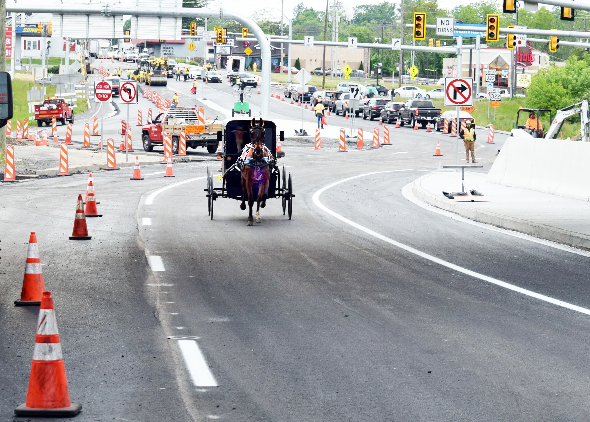 An image of a horse and buggy under a bridge navigating its way through a work zone with orange cones and orange and white work zone barricades as the Diverging Diamond Interchange at the 322/222 interchange was being completed
